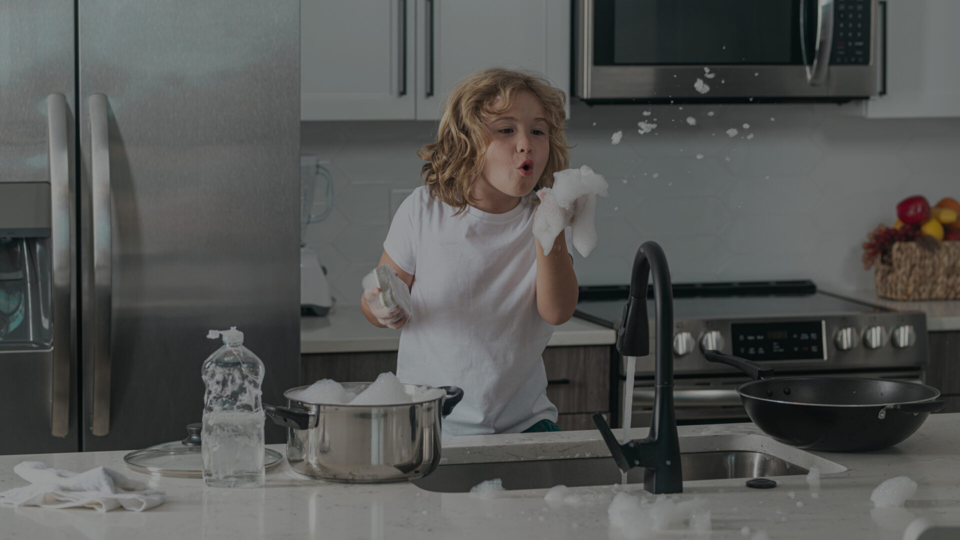 Child washing dishes near sink in kitchen. Child with sponge with dish washing liquid is doing the dishes at home kitchen by using wash sponge and dish washing.